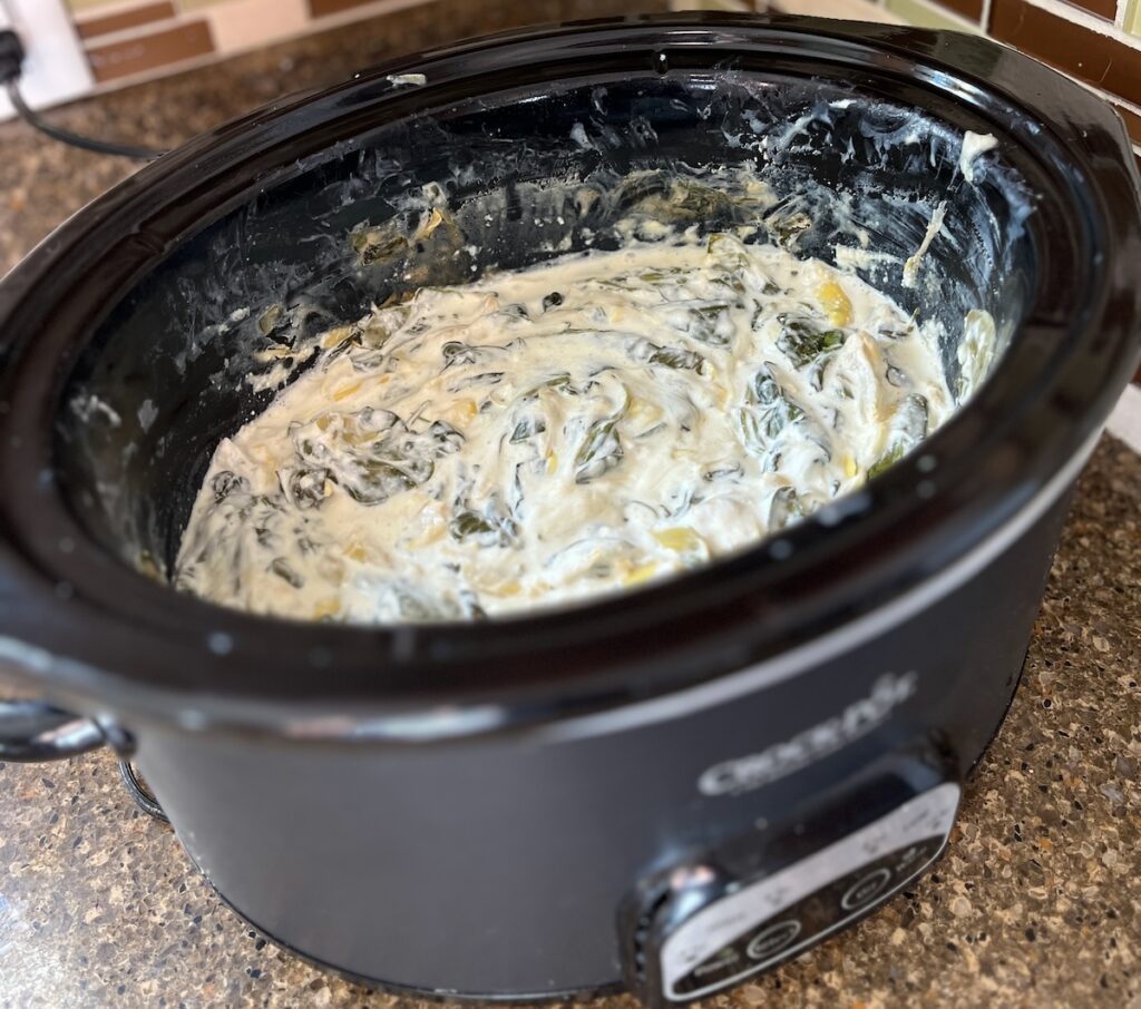 A slow cooker brimming with low carb spinach artichoke dip sits invitingly on the kitchen counter, creamy and ready to enjoy.