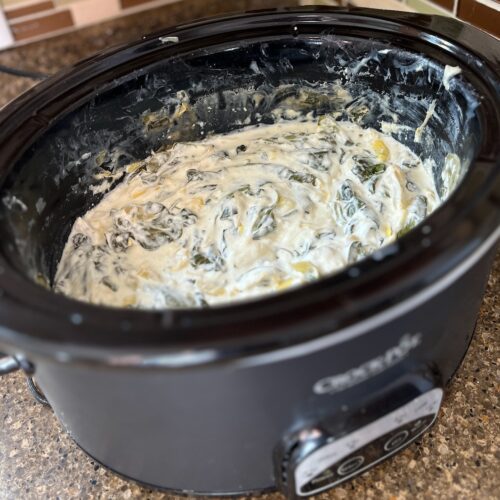 A slow cooker brimming with low carb spinach artichoke dip sits invitingly on the kitchen counter, creamy and ready to enjoy.