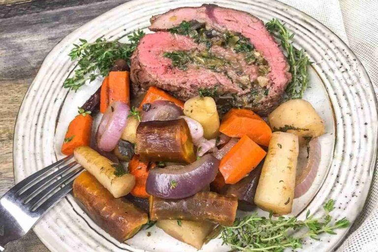 Plate of stuffed beef roulade with roasted carrots, onions, and parsnips, garnished with fresh herbs.