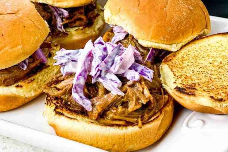 Three pulled pork sliders topped with coleslaw on toasted buns, served on a white plate.