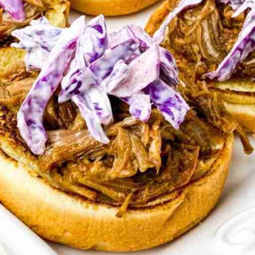 Open-faced sandwich with pulled pork and purple coleslaw on a toasted bun.