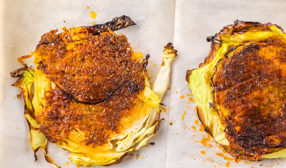 Two roasted cabbage steaks on a parchment-lined baking sheet, seasoned and browned on the edges.