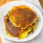 Grilled cabbage steaks on a white plate, garnished with chopped herbs, resting on a striped cloth.