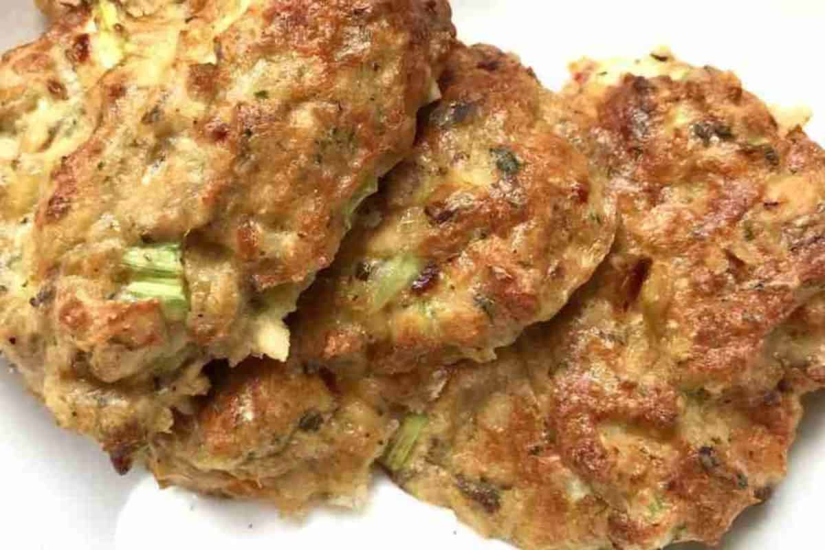 Close-up of three cooked, golden-brown patties with visible herbs and green bits, on a white plate.