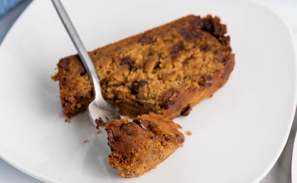 A slice of banana bread with chocolate chips on a white plate, with a fork taking a piece.