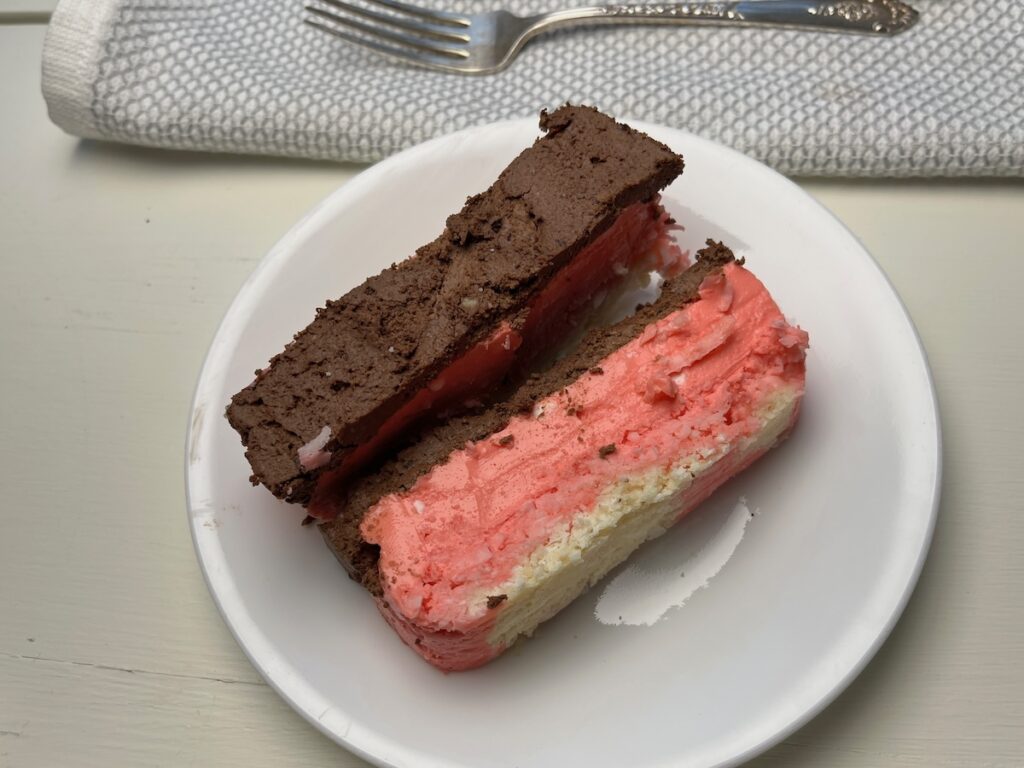 Two slices of layered cake, one chocolate and one pink with white frosting, on a white plate. A fork rests on a folded napkin in the background.