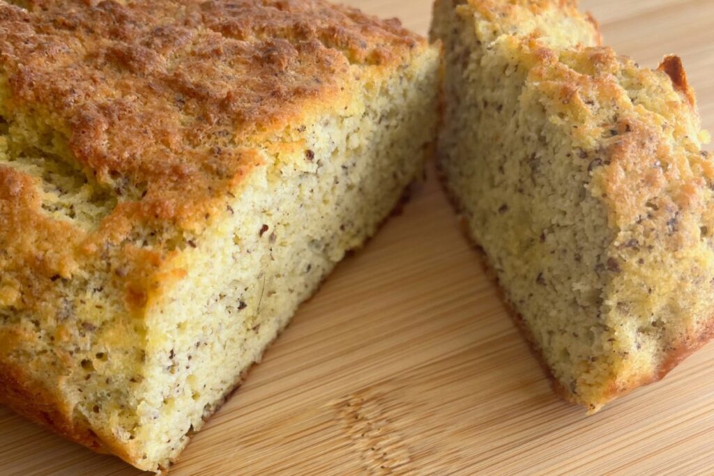 A loaf of banana bread on a wooden surface, with a slice cut from it.