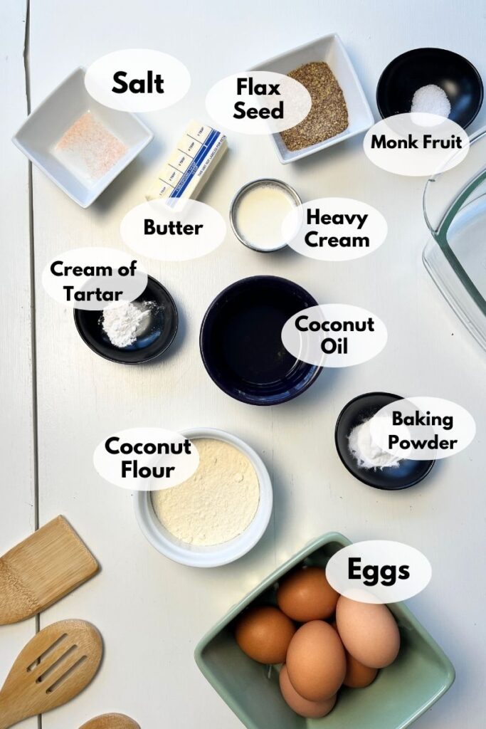Ingredients on a table include salt, flax seed, monk fruit, butter, heavy cream, cream of tartar, coconut oil, baking powder, coconut flour, and eggs.