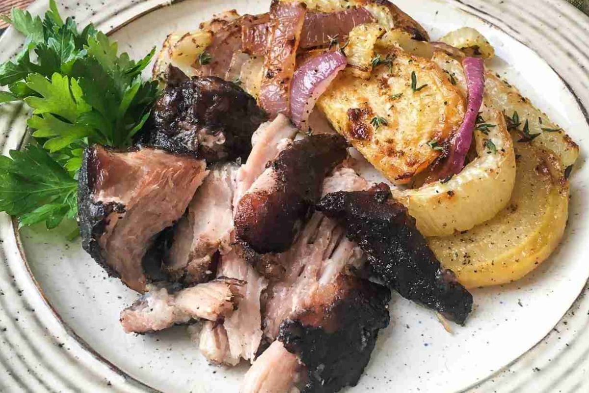 Plate with sliced roasted meat, roasted potatoes with red onions, and a sprig of fresh parsley, served on a white dish.