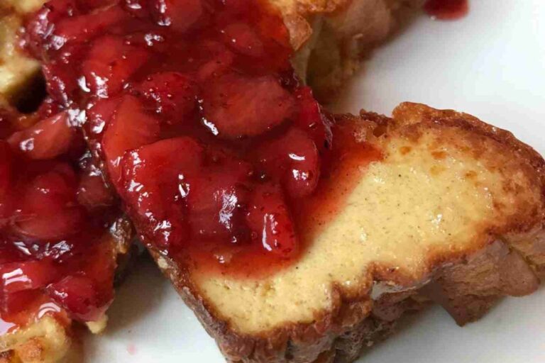 Close-up of meatless French toast slices topped with chunky strawberry sauce on a white plate.