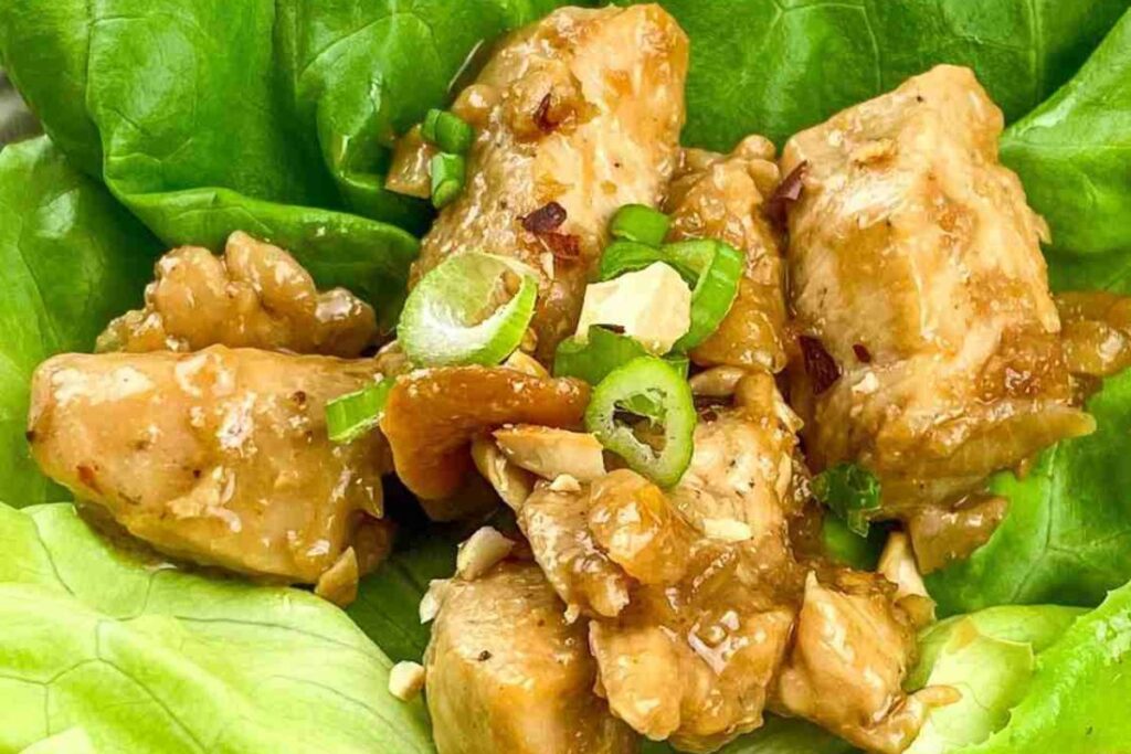 Chunks of cooked chicken with sauce and chopped green onions served on a fresh green lettuce leaf.