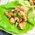 Chicken pieces with cashews and sliced green onions served on fresh lettuce leaves, with a small bowl of chopped green onions and some cashews on the side.