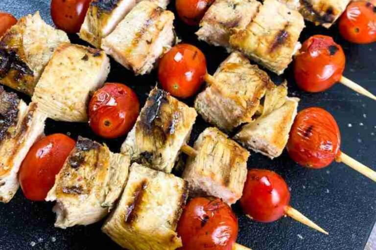 Grilled chicken and cherry tomatoes on wooden skewers, arranged on a dark surface.