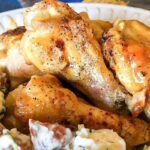 Keto chicken wings seasoned with pepper, served on a white plate alongside a fresh, herbed potato salad.