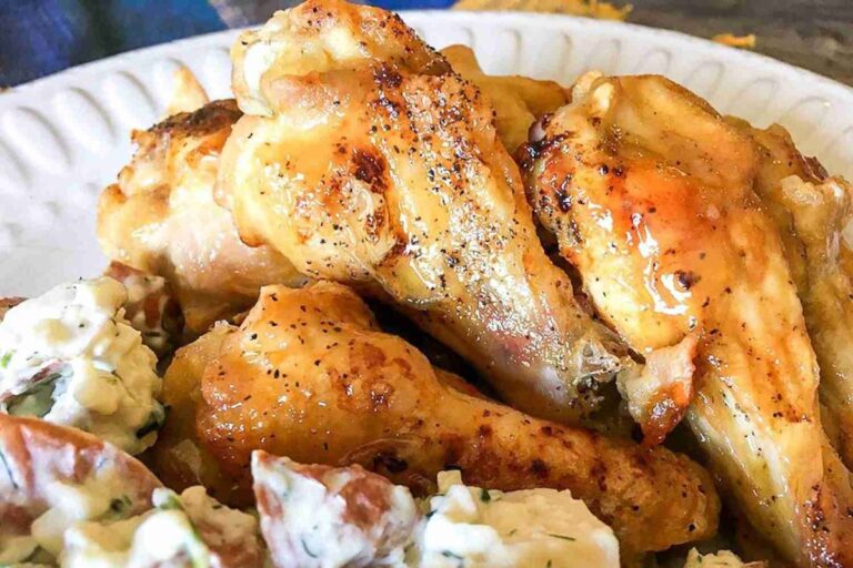 Keto chicken wings seasoned with pepper, served on a white plate alongside a fresh, herbed potato salad.