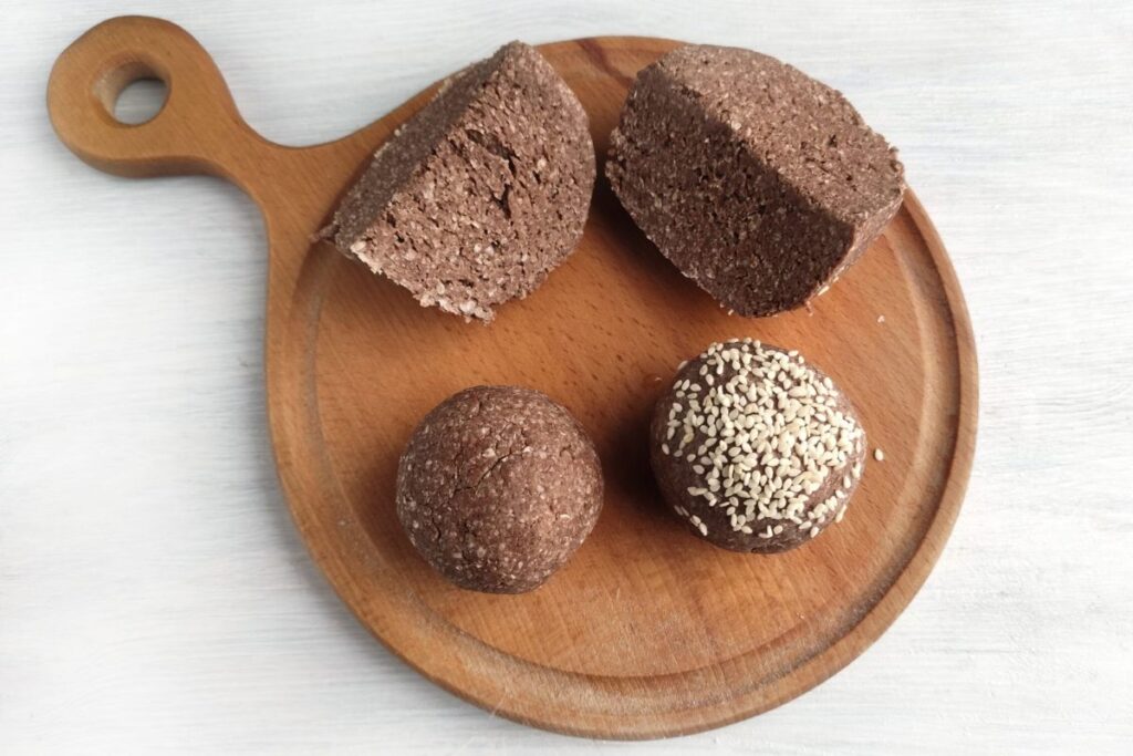Four pieces of chocolate dessert, two rectangular slices and two round balls, one with seeds, on a wooden serving board.