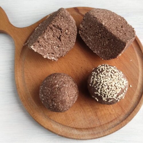 Four pieces of chocolate dessert, two rectangular slices and two round balls, one with seeds, on a wooden serving board.