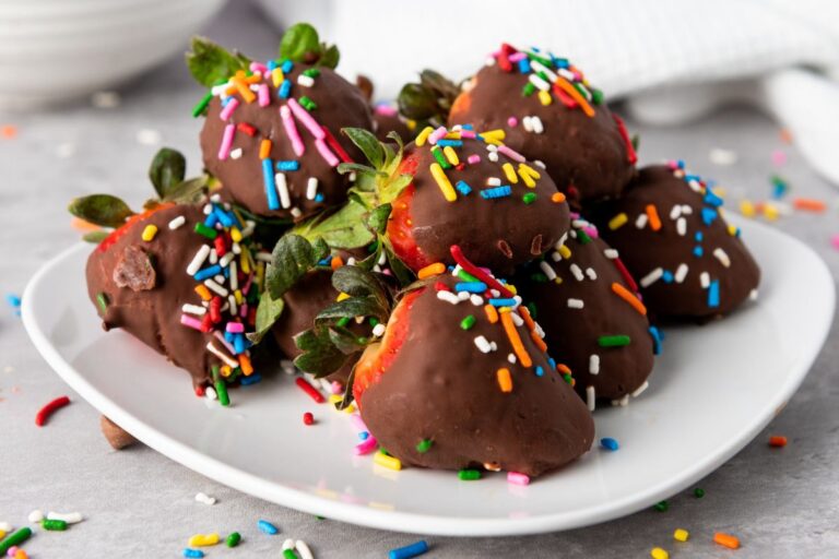 A plate of chocolate-covered strawberries topped with colorful sprinkles on a light gray surface.