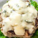 A cooked beef and sausage blue cheese burger patty topped with melted cheese sits on a bed of green leaf lettuce.