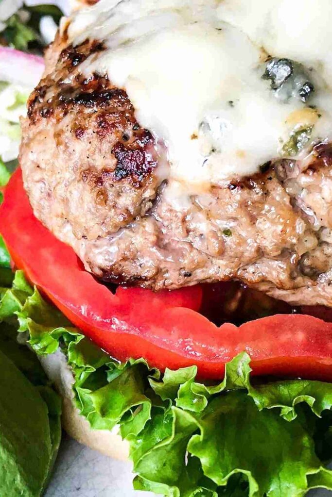 Close-up of a cheeseburger with melted cheese on a beef patty, sliced tomato, and leaf lettuce on a bun.