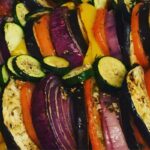 Sliced zucchini, eggplant, red onion, and tomato arranged in rows and seasoned with herbs and spices, ready for roasting.