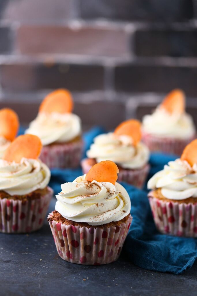 Frosted keto carrot cake cupcakes arranged on a dark surface with a soft, blurred background.