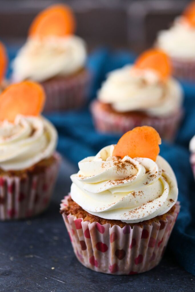 Close-up of a keto carrot cake cupcake with swirled cream cheese frosting and carrot decoration.