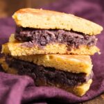 Two dorayaki pancakes filled with sweet red bean paste are stacked on a purple cloth.