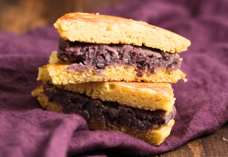 Two dorayaki pancakes filled with sweet red bean paste are stacked on a purple cloth.