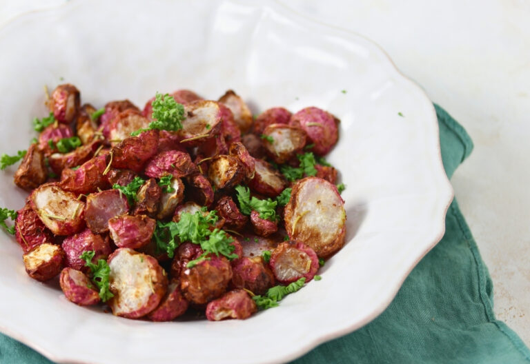 A white plate with roasted radish pieces garnished with chopped parsley, placed on a green cloth napkin.