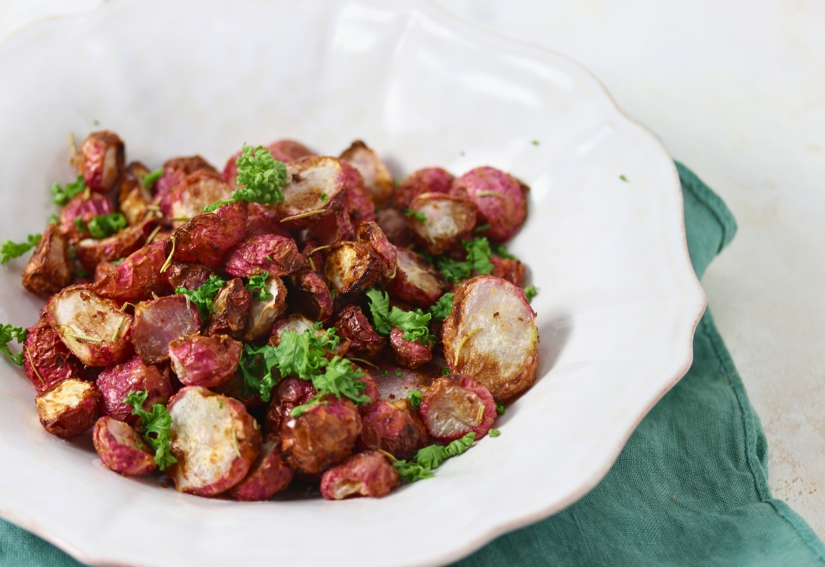 A white plate with roasted radish pieces garnished with chopped parsley, placed on a green cloth napkin.
