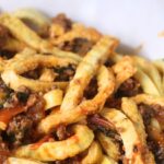 Close-up of pasta noodles mixed with ground meat, vegetables, and tomato sauce on a white plate.